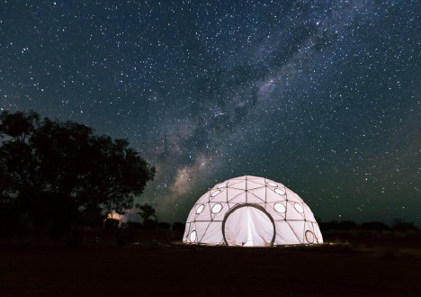 A brightly lit dome tent under a star studded night sky.