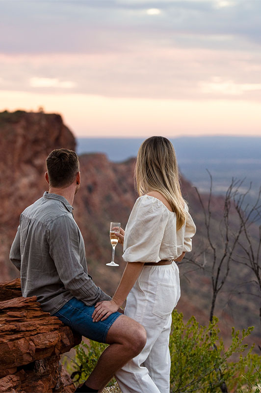 A couple enjoys drinks while looking across the landscape of the Outback.