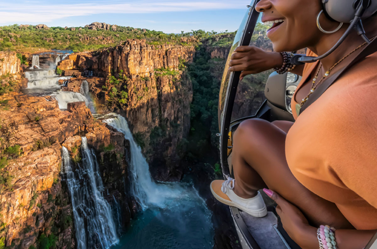 A woman thrills to the view of dramatic waterfalls from a helicopter.