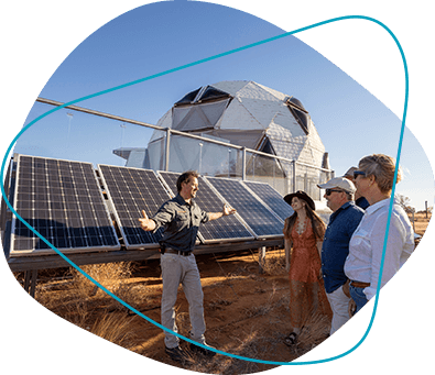 A group of friends listen to a man discussing the solar panels behind him.