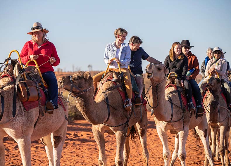 A group of people riding camels follow a guide.