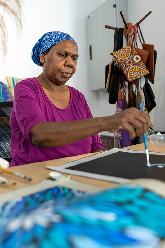 An Aboriginal woman paints in a studio.