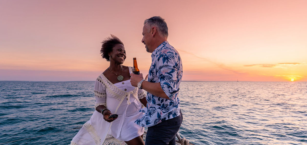 A couple enjoys each other's company on a boat as the sun sets over the ocean.