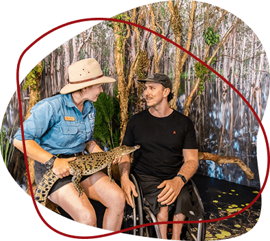 A guide shows a baby alligator to a man in a wheelchair